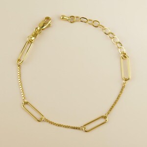 May include: A gold-colored bracelet featuring a mix of chain styles. The bracelet includes rectangular links, a box chain, and a series of small oval links for adjustability. It has a lobster clasp closure.