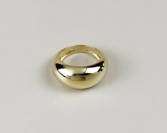 May include: A gold-colored ring with a rounded, smooth design. The ring has a thick band and a polished, reflective surface. The jewelry piece is set against a plain, light background.