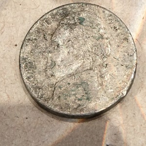 Puede incluir: Una moneda de plata con un retrato de una persona en el anverso. La moneda está desgastada y tiene una pátina verde.
