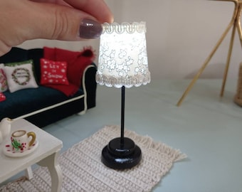May include: A miniature white lamp with a floral pattern on the shade. The lamp has a black base and is sitting on a white rug.