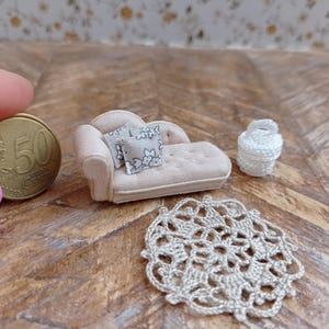May include: Miniature dollhouse furniture set including a beige chaise lounge with two floral pillows, a white crocheted basket, and a crocheted doily. A 50-cent coin is included for scale. The items are on a wooden surface.