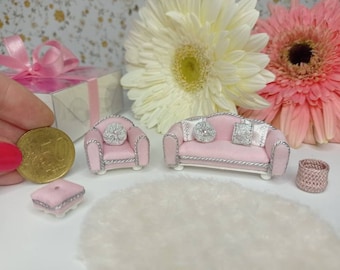 May include: A pink miniature living room set with a sofa, two armchairs, a footstool, and a small basket. The furniture is decorated with silver trim and has pink cushions.