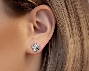May include: A pair of silver flower-shaped stud earrings. The earrings are small and delicate, with a detailed design.