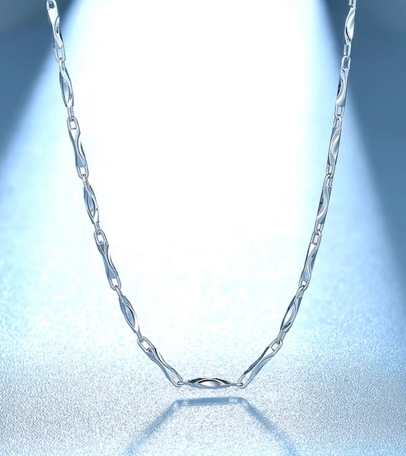May include: A silver chain necklace with a unique, wavy link design. The chain is made of metal and has a polished finish.