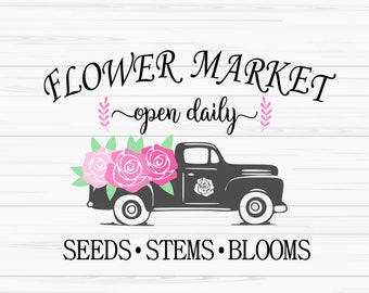 May include: A black pickup truck with pink roses in the bed. The truck has the words "FLOWER MARKET open daily" above it and "SEEDS STEMS BLOOMS" below it.