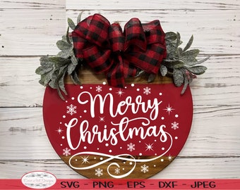 Pode incluir: Um sinal redondo de madeira marrom e vermelho com uma inscrição branca em itálico que diz "Feliz Natal". O sinal é decorado com um laço vermelho e preto xadrez e folhagem verde.
