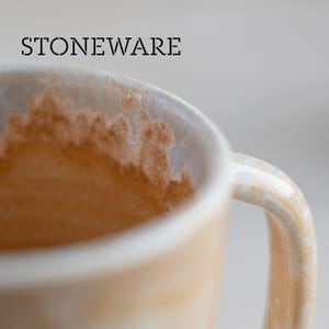 May include: Close-up of a stoneware mug with a handle. The mug has a light beige color with brown stains inside. The word "STONEWARE" is printed in black at the top of the image.