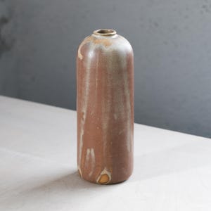 May include: A brown ceramic vase with a light brown glaze. The vase has a rounded bottom and a narrow opening at the top.