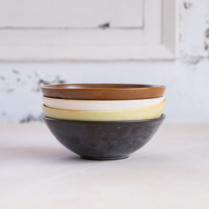 May include: A stack of three ceramic bowls. The top bowl is brown, the middle bowl is white, and the bottom bowl is black.