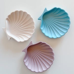 Può includere: Tre piatti decorativi a forma di conchiglia in bianco, azzurro e lilla chiaro.