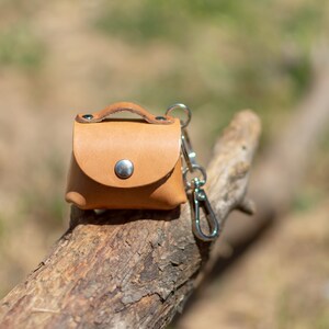 May include: A small, brown leather keychain with a metal clasp. The keychain is shaped like a small purse and has a metal button on the front.