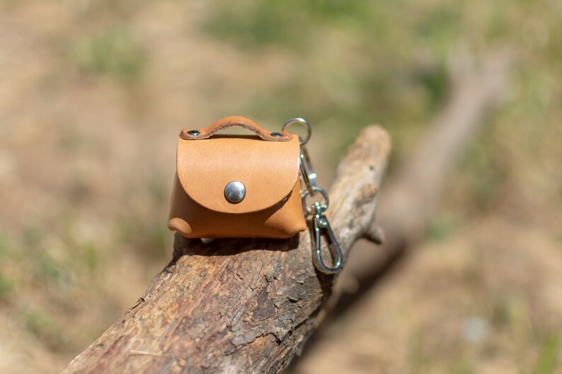 May include: A small, brown leather keychain with a metal clasp. The keychain is shaped like a small purse and has a metal button on the front.