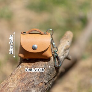 May include: A small, light brown leather keychain purse with a silver clasp and a silver key ring. The purse measures 4 inches tall and 6 inches wide.