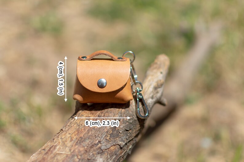 May include: A small, light brown leather keychain purse with a silver clasp and a silver key ring. The purse measures 4 inches tall and 6 inches wide.