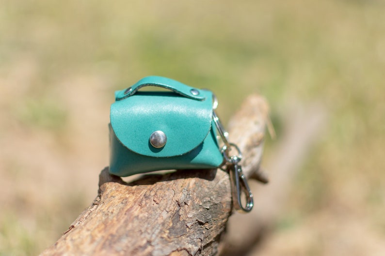 May include: A small teal leather purse with a silver clasp and a silver key chain attached.