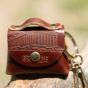 May include: A brown leather keychain with a gold metal ring and clasp. The keychain features an embossed image of a Greek temple and the word "GREECE".