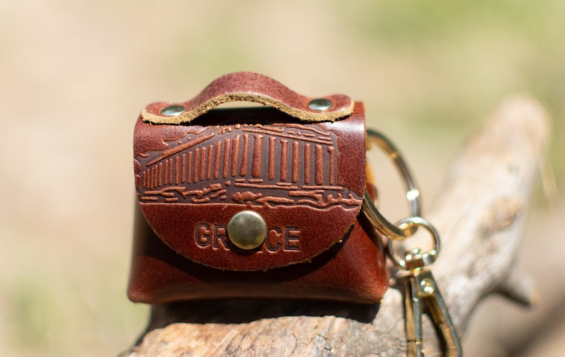 May include: A brown leather keychain with a gold metal ring and clasp. The keychain features an embossed image of a Greek temple and the word "GREECE".