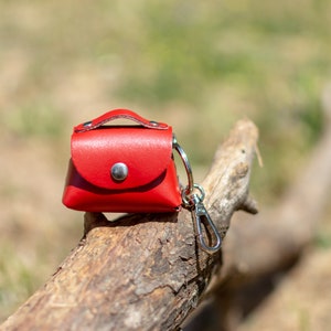 May include: A small red leather purse keychain with a silver clasp. The keychain is sitting on a piece of weathered wood.