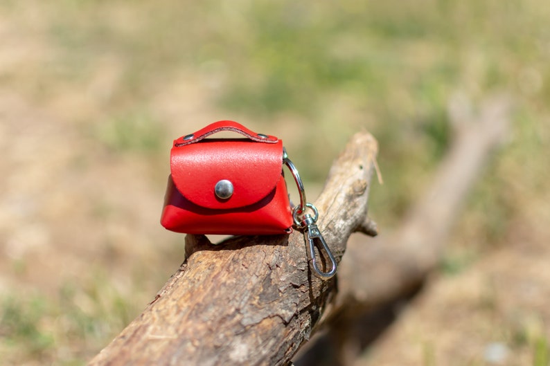 May include: A small red leather purse keychain with a silver clasp. The keychain is sitting on a piece of weathered wood.