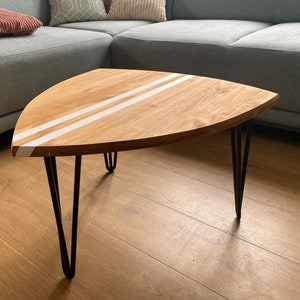 Puede incluir: Una mesa de centro de madera con una forma única de tabla de surf y dos rayas blancas pintadas en la parte superior. La mesa tiene patas de horquilla negras.