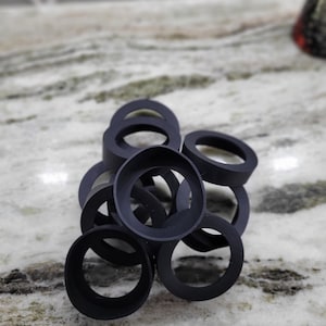 May include: A group of black rubber rings stacked on top of each other. The rings are all the same size and shape.