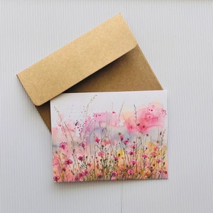 May include: A blank greeting card with a watercolor illustration of a field of pink wildflowers. The card is in a brown envelope.