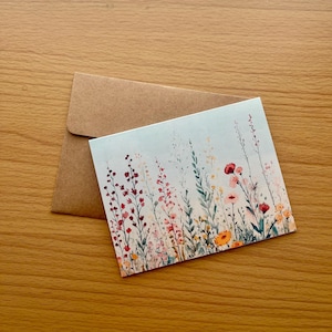 May include: A card with a watercolor illustration of a field of wildflowers in shades of pink, red, orange, and yellow. The flowers are on a light blue background.