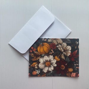 May include: A card with a floral design featuring white, red, and yellow flowers, leaves, and a pumpkin on a dark background.
