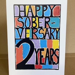 May include: A colorful card with the text "Happy Soberversary 2 Years" in black lettering. The text is surrounded by a colorful mosaic of squares.