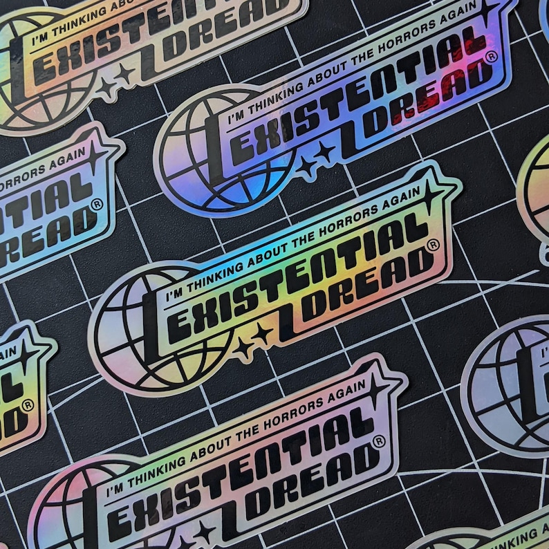 May include: Holographic stickers with the text "I'M THINKING ABOUT THE HORRORS AGAIN" and "EXISTENTIAL DREAD" in a bold, stylized font. The design includes a globe and star accents. The stickers have a rainbow sheen and are on a black grid background.