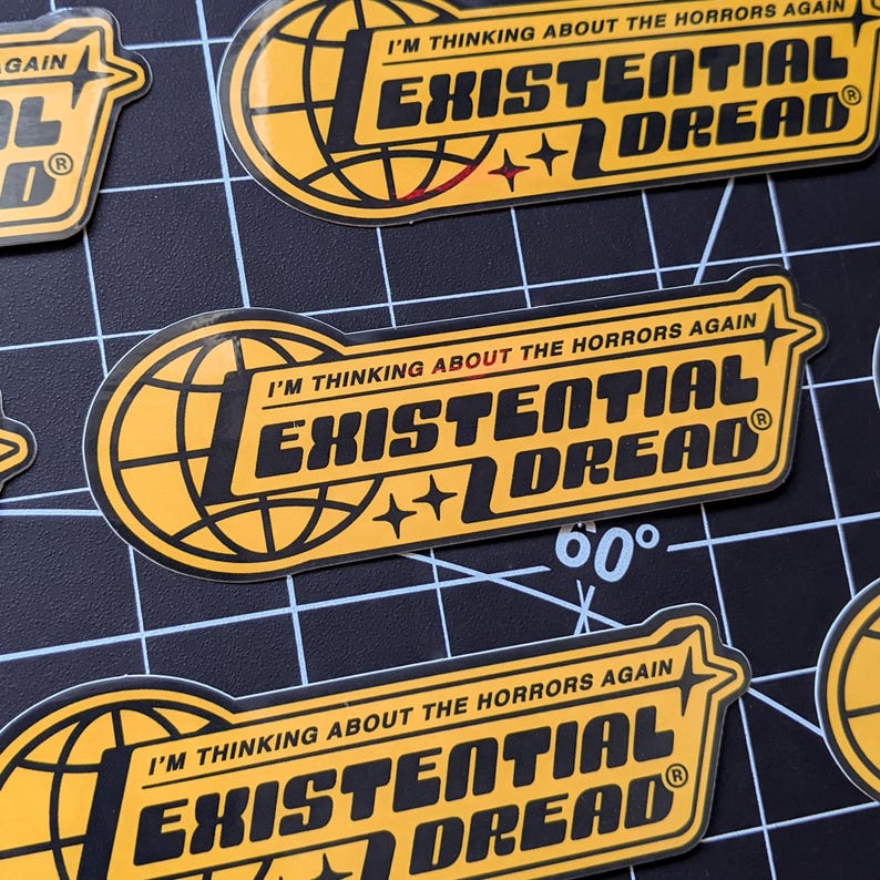 May include: Yellow and black stickers with the text "I'M THINKING ABOUT THE HORRORS AGAIN" and "EXISTENTIAL DREAD". The stickers feature a globe design and star accents. The stickers are on a black grid surface.