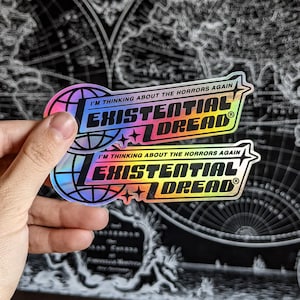 May include: Two holographic stickers with the text "I'M THINKING ABOUT THE HORRORS AGAIN" and "EXISTENTIAL DREAD" in black and rainbow colors. The stickers have a globe and star design.