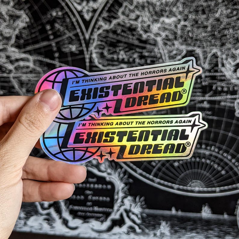 May include: Two holographic stickers with the text "I'M THINKING ABOUT THE HORRORS AGAIN" and "EXISTENTIAL DREAD" in black and rainbow colors. The stickers have a globe and star design.