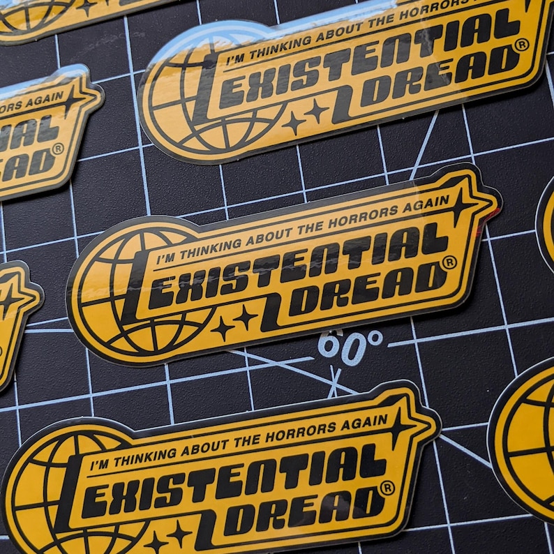 May include: Yellow and black stickers with the text "I'M THINKING ABOUT THE HORRORS AGAIN" and "EXISTENTIAL DREAD". The stickers feature a globe design and star accents. The stickers are on a black grid.
