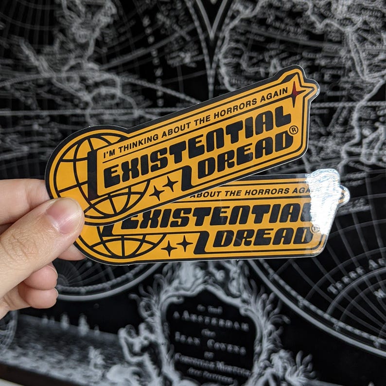 May include: Two yellow and black stickers with the words "EXISTENTIAL DREAD" in bold, stylized font. The top sticker reads "I'M THINKING ABOUT THE HORRORS AGAIN." The bottom sticker reads "ABOUT THE HORRORS AGAIN."