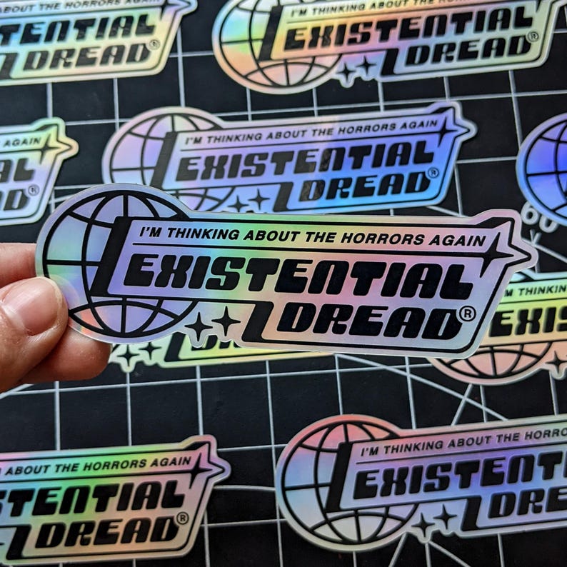 May include: Holographic stickers with the text "I'M THINKING ABOUT THE HORRORS AGAIN" and "EXISTENTIAL DREAD" in a stylized font. The design includes a globe and star accents. The stickers have a reflective, iridescent finish.