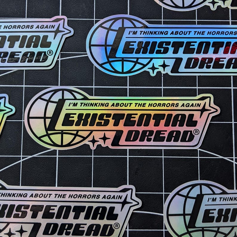 May include: Holographic stickers with the text "I'M THINKING ABOUT THE HORRORS AGAIN" and "EXISTENTIAL DREAD" in a stylized font. The design includes a globe and star accents. The stickers are on a black grid background.