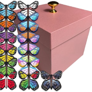 May include: A pink gift box with a gold knob on the lid. The box is surrounded by a variety of colorful butterfly toys with black wings.