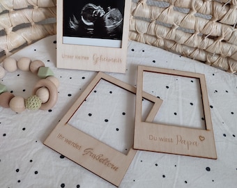 May include: Three wooden photo frames with text. The top frame shows a black and white ultrasound image with the text "Unser kleines Geheimnis". The left frame has the text "Ihr werdet Grosseltern" and the right frame has the text "Du wirst Papa".