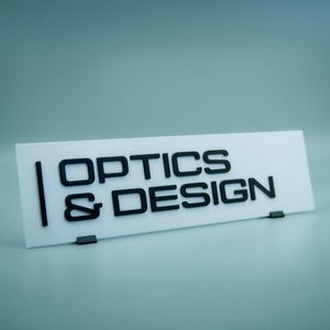 Op de afbeelding: Een wit bord met zwarte tekst die "OPTICS & DESIGN" zegt.