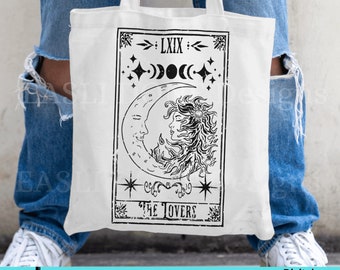 May include: A white tote bag with a black and white illustration of a tarot card. The card is labeled "LXIX" and "THE LOVERS". The illustration features a crescent moon with a face and a sun with a face.