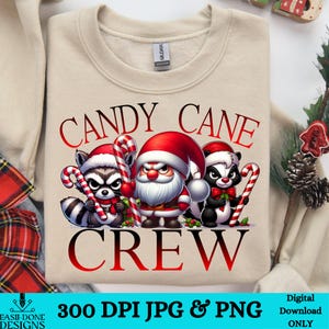 Op de afbeelding: Een beige sweatshirt met de tekst "CANDY CANE CREW" in rood. Het ontwerp bevat een cartoon kerstman, een wasbeer en een stinkdier die snoepstokken vasthouden.