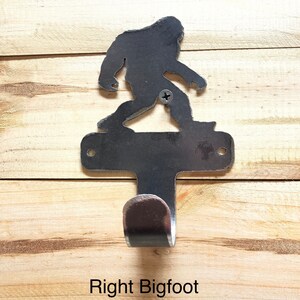 Op de afbeelding: Een metalen wandhaak in de vorm van een Bigfoot-silhouet. De haak is zilverkleurig en heeft een enkele haak aan de onderkant. De tekst "Right Bigfoot" is onder de haak afgedrukt.