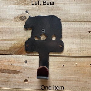 Op de afbeelding: Zwarte metalen beren-silhouet wandhaak met een enkele haak aan de onderkant. De beer kijkt naar links en de tekst "Left Bear" staat boven de beer. De tekst "One item" staat onder de haak.