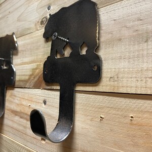 Op de afbeelding: Een metalen beren-silhouet wandhaak met een rustieke afwerking. De haak is bevestigd aan een houten muur met een schroef.