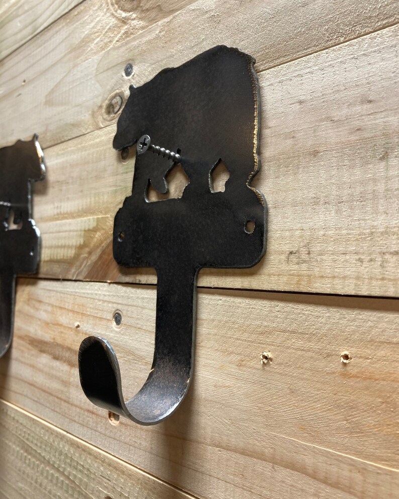 Op de afbeelding: Een metalen beren-silhouet wandhaak met een rustieke afwerking. De haak is bevestigd aan een houten muur met een schroef.