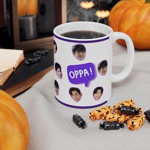 May include: White ceramic coffee mug with a purple border and multiple images of men's faces. The text "OPPA!" is written in a purple speech bubble.