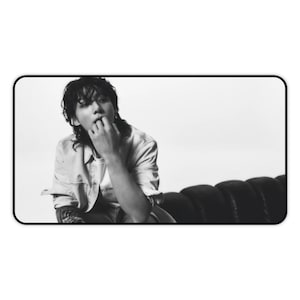 Könnte beinhalten: Ein Schwarzweißfoto einer Person, die auf einem Sofa sitzt. Die Person trägt ein Hemd mit Knöpfen und hat langes Haar.