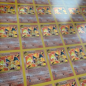Puede incluir: Una hoja de cartas coleccionables de Charizard. Cada carta presenta una imagen holográfica del Pokémon de tipo fuego. Las cartas tienen un borde amarillo e incluyen texto como "Charizard" y "120 HP".
