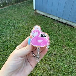May include: Pink flamingo pool float with glitter and the word "FLOAT" on it. The float is attached to a clear plastic badge holder with a spring clip.